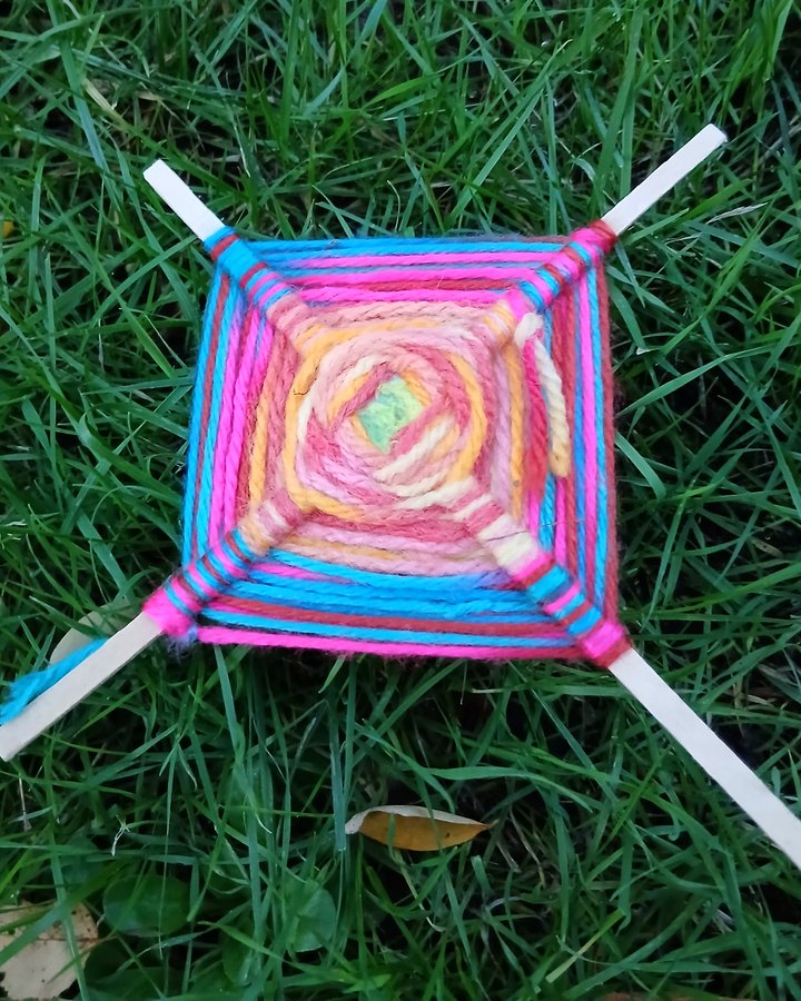 A bright woolly God's eye, woven in pink, blue and sunshine yellow